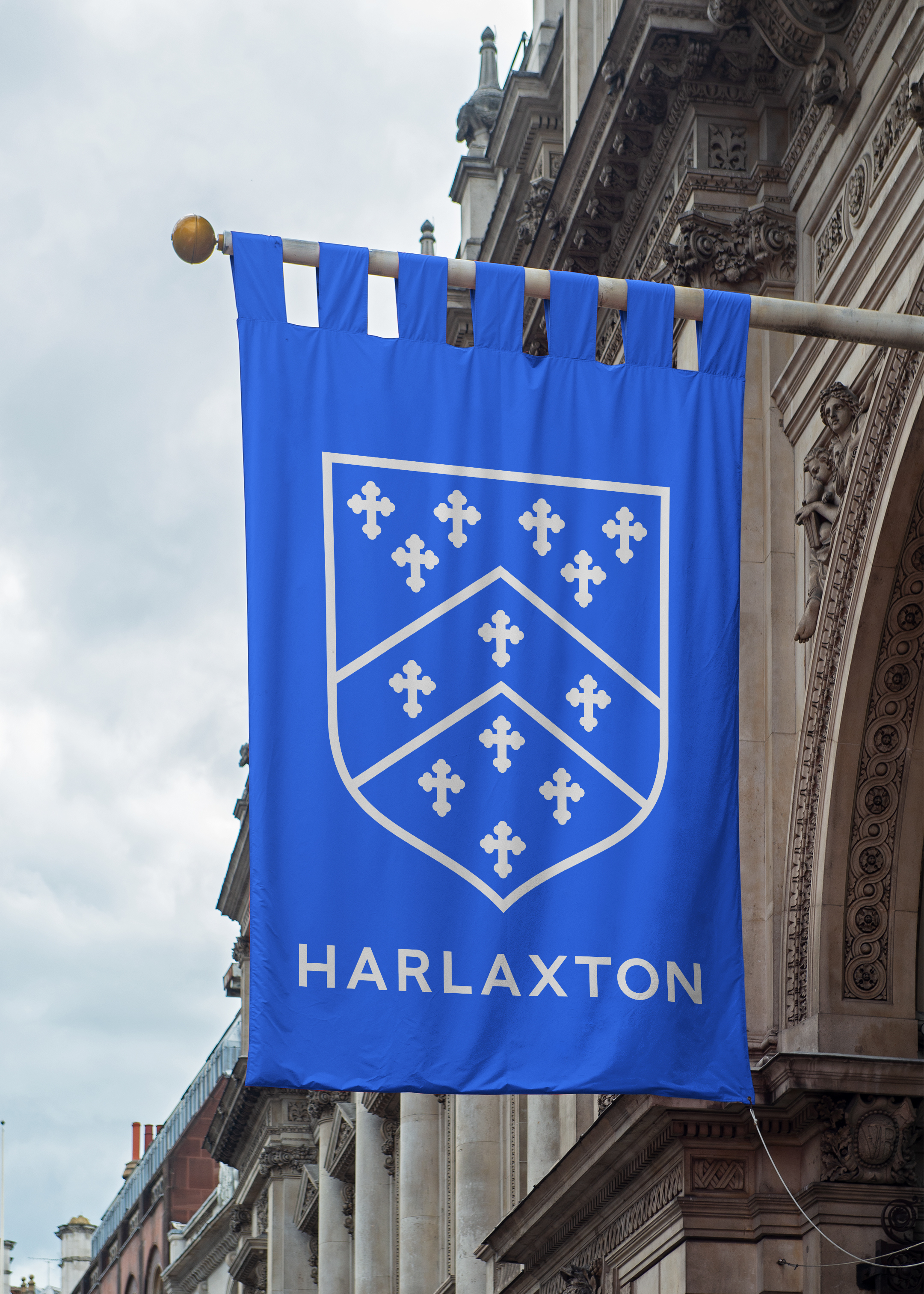 Bright blue fabric banner hanging from a pole, with a large light grey Harlaxton logo and shield on.