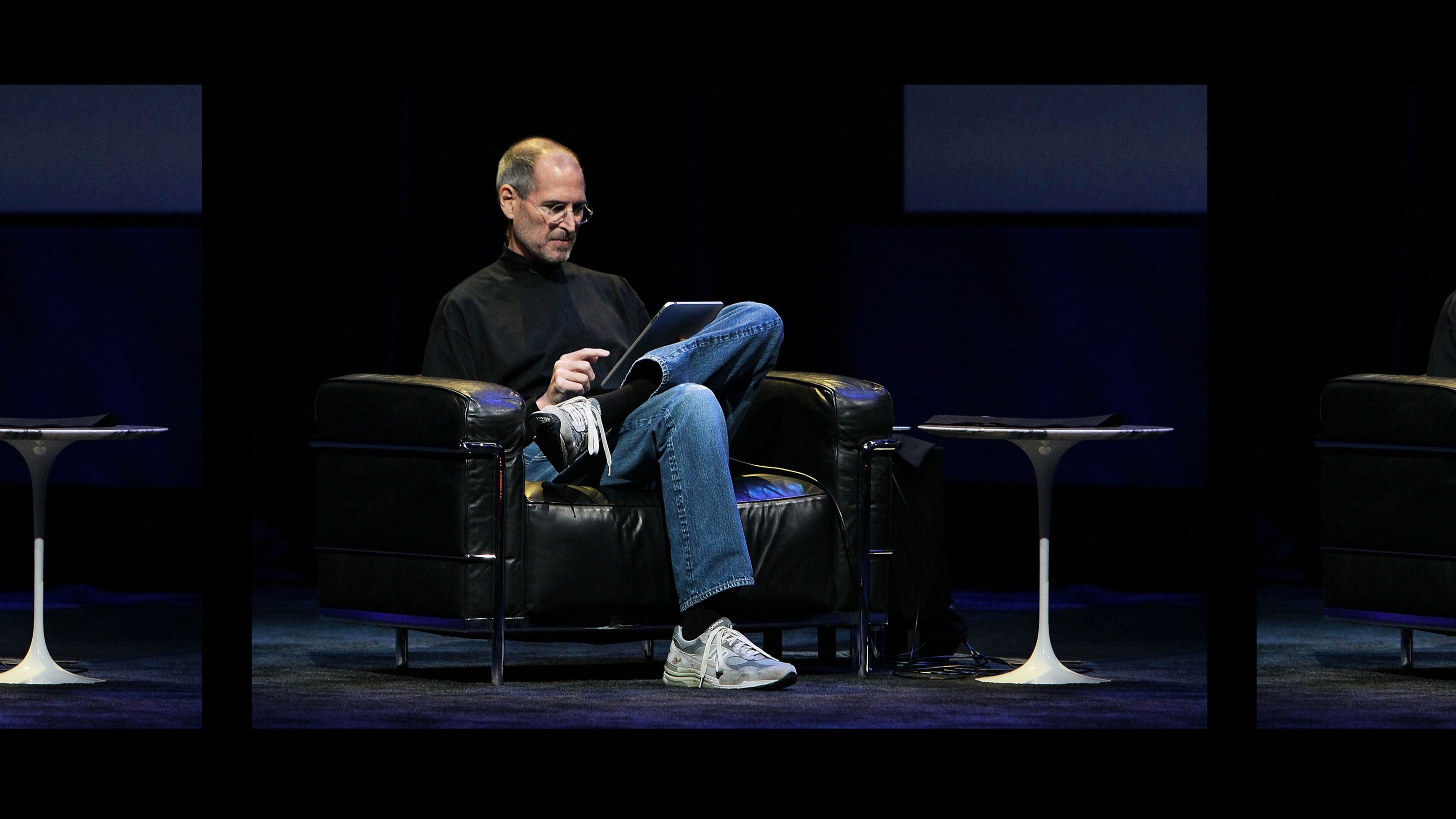 Steve Jobs on stage using an IPad, wearing New Balance trainers