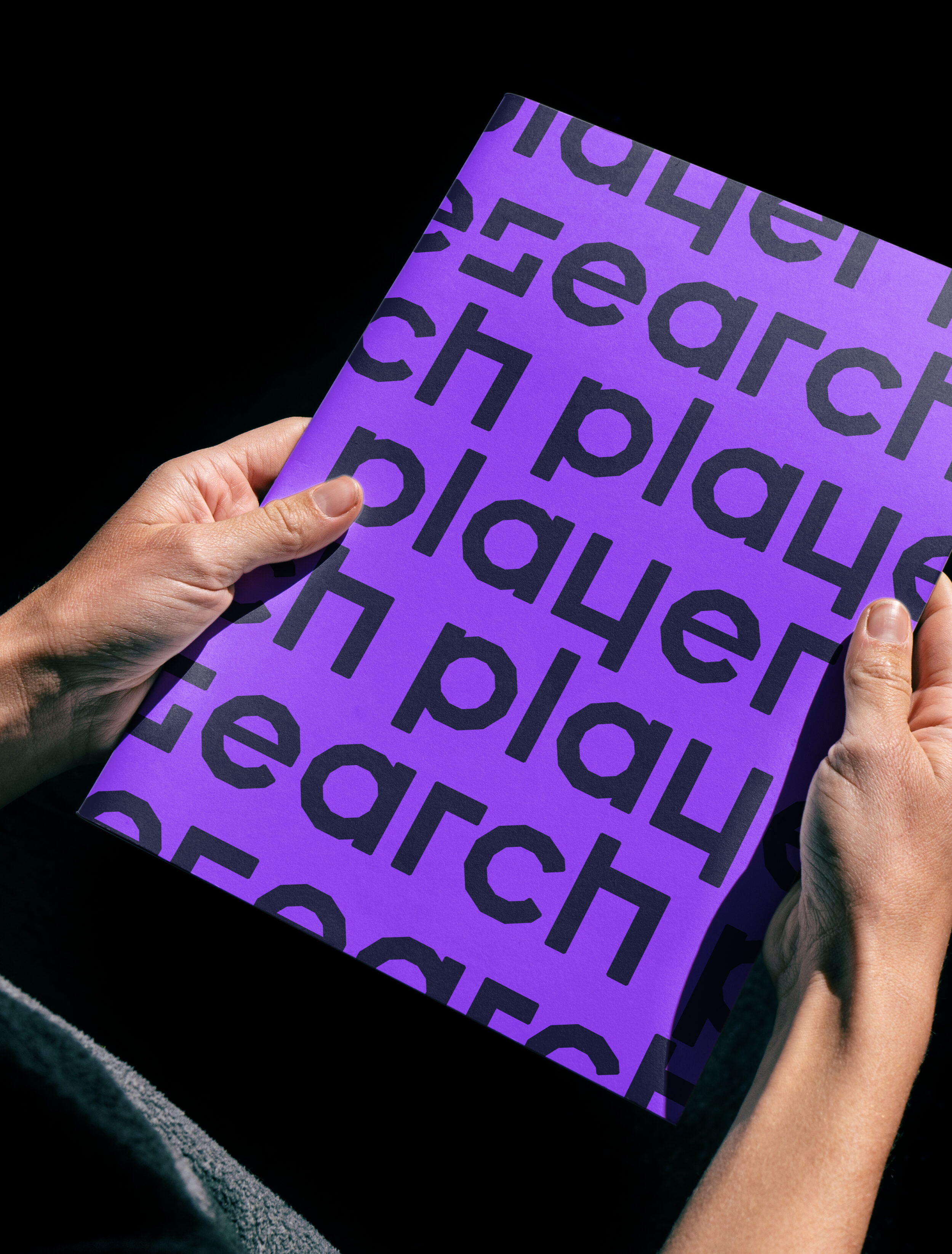 hands holding purple brochure with player research logo printed on it