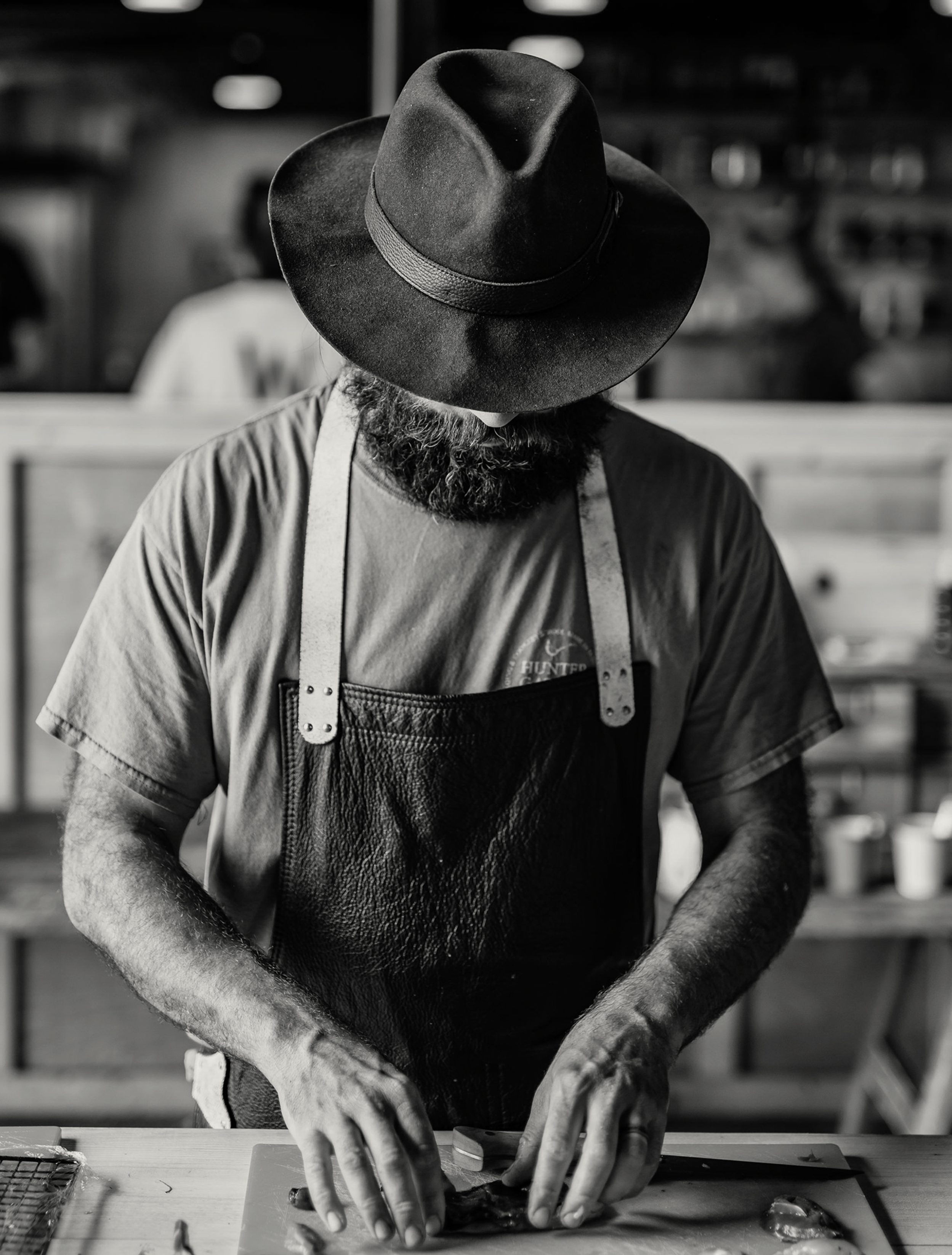 Black and white photo of a bearded man cutting up meat