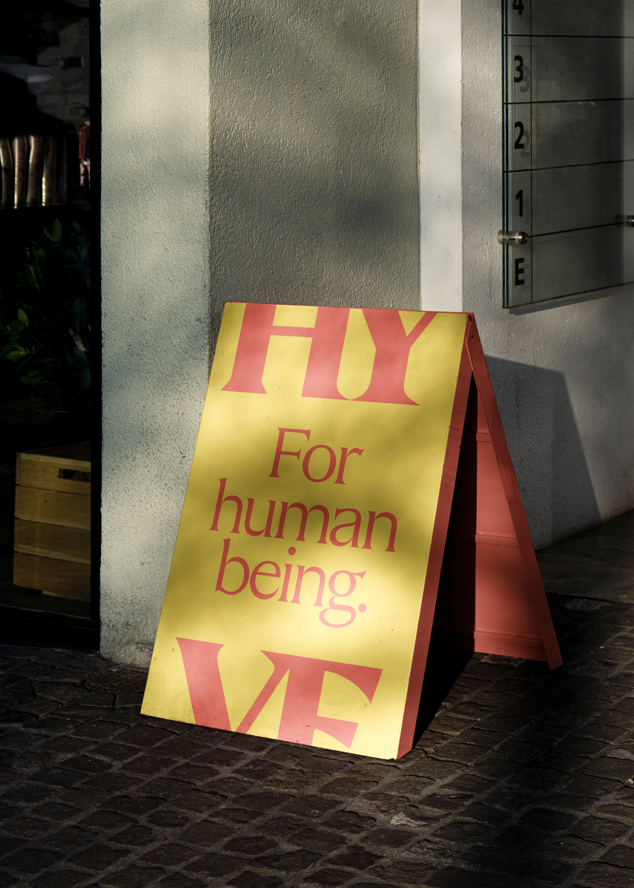 'For human being' large type a-board in red on a yellow background, framed with a HY at the top and VE at the bottom.
