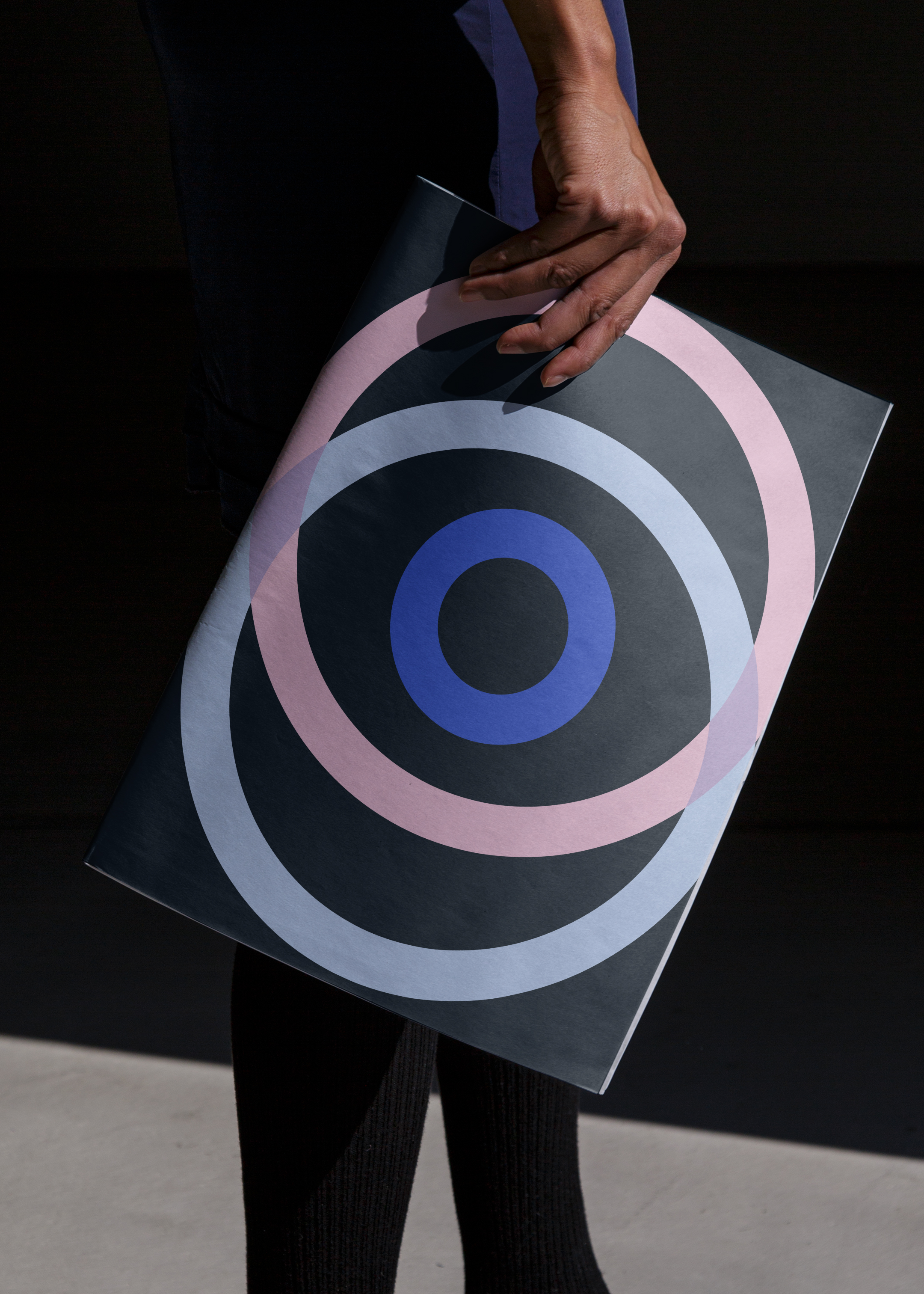 A man holds a close newspaper by his side. The one side that is visible has two circles eclipsing one another like a ven diagram with a third circle in the middle. It looks almost like an eye.