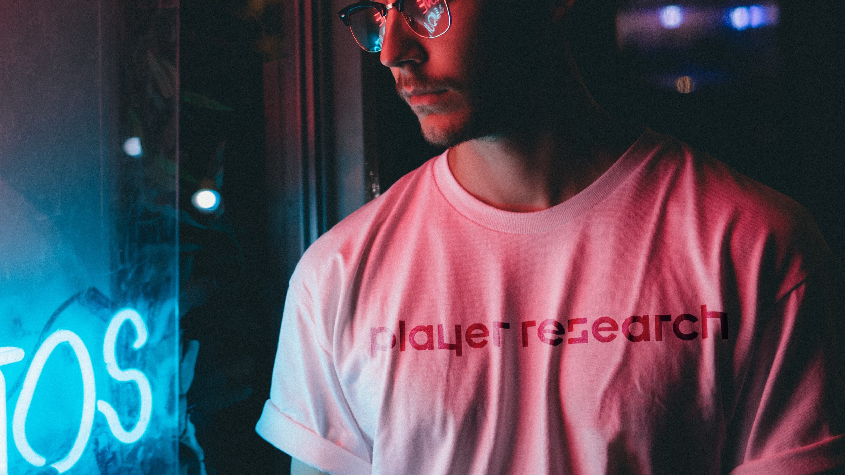 Player Research logo on a white t-shirt worn by a young male, standing next to a blue neon sign
