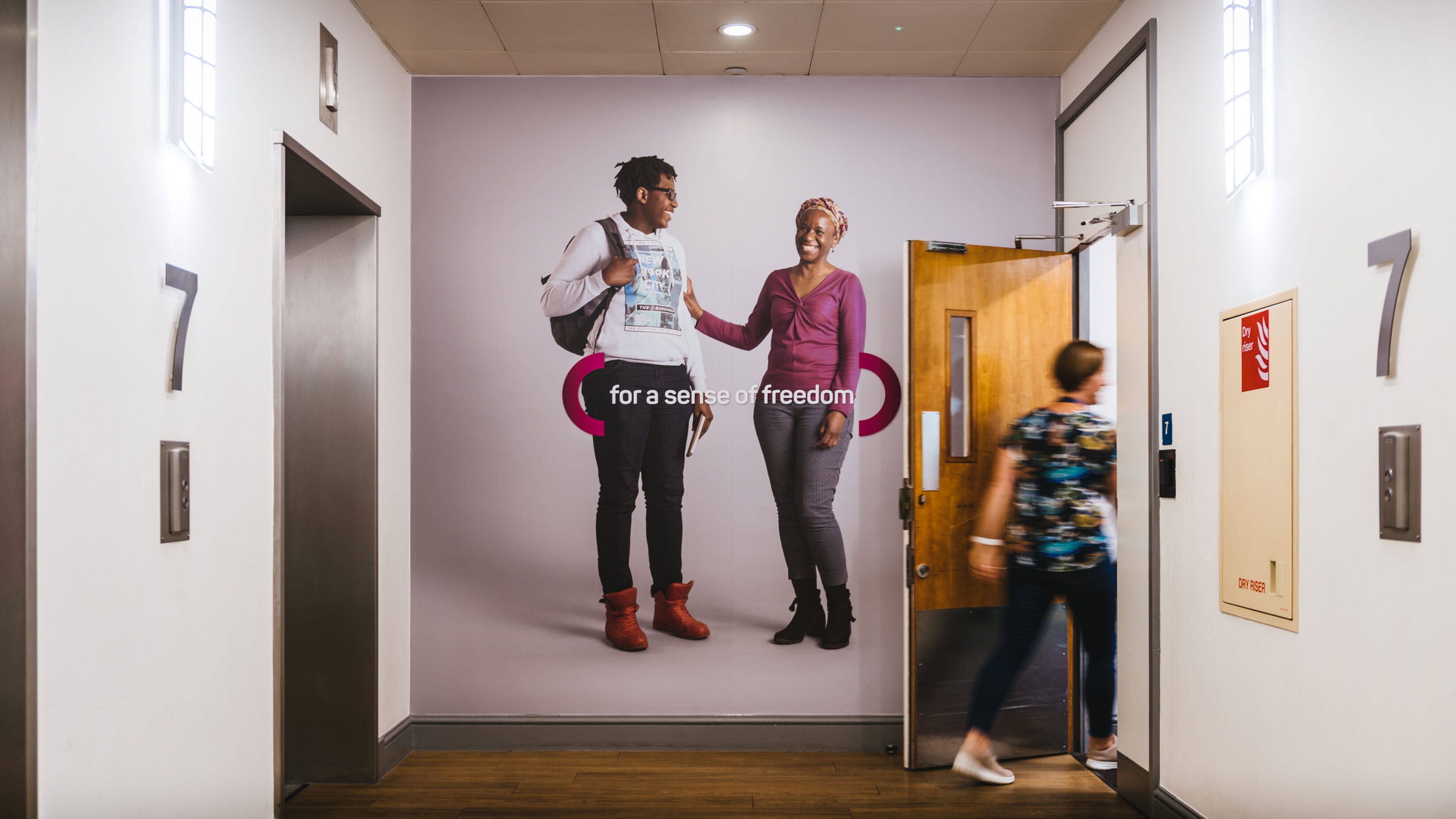 Wall graphic showing a mother and son photographed on a grey background, with the message 'for a sense of freedom' placed over the centre of the wall
