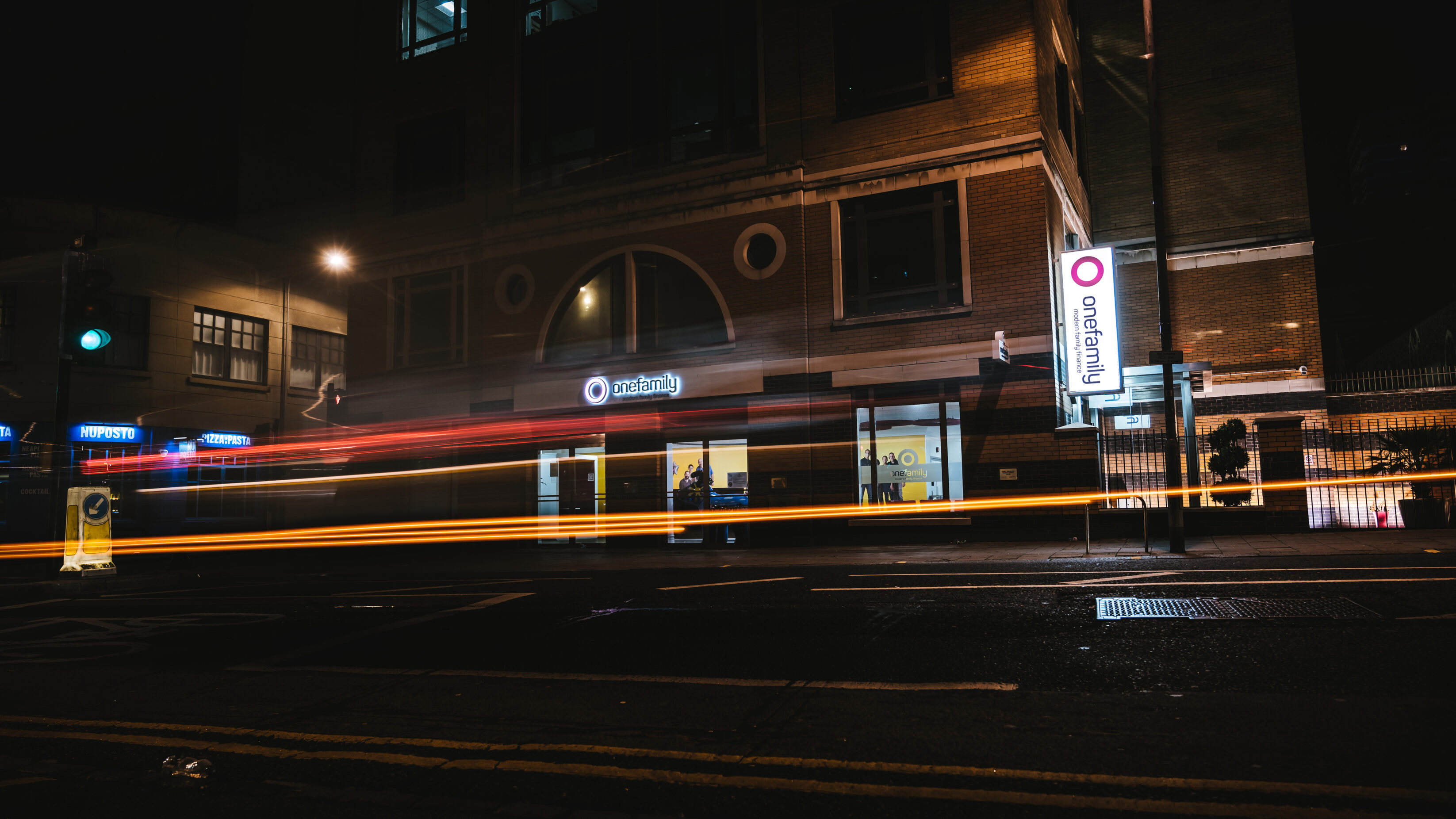 External photograph of the office taken at night with a slow shutter speed, to show the illuminated logo, lightbox and light trails.