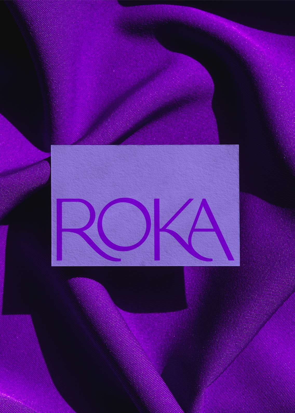 Business card with a large ROKA logo on, sitting on a purple velvet material