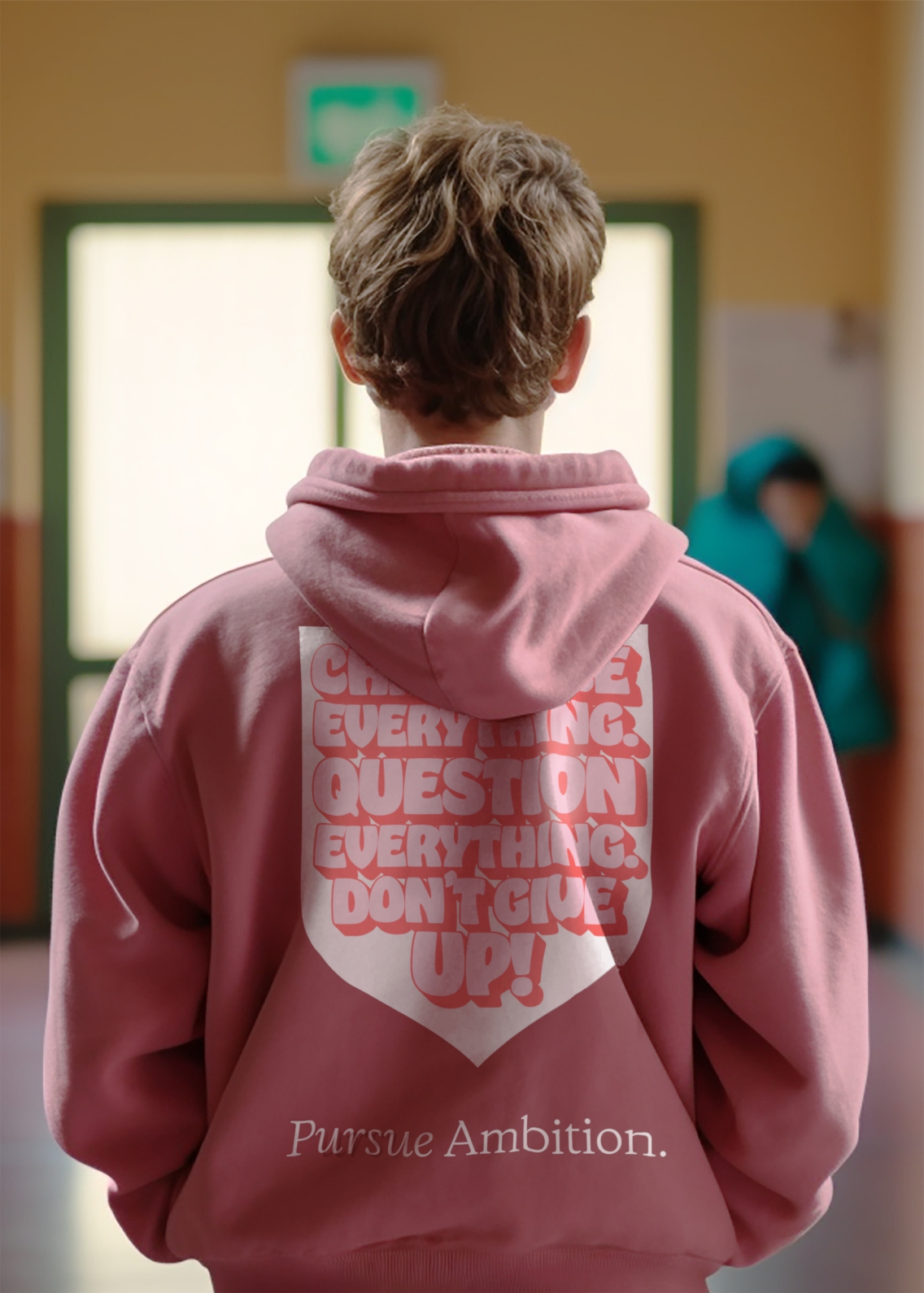 View from the back of a young male wearing a dark pink hoodie, with a large shield and Pursue Ambition type on.