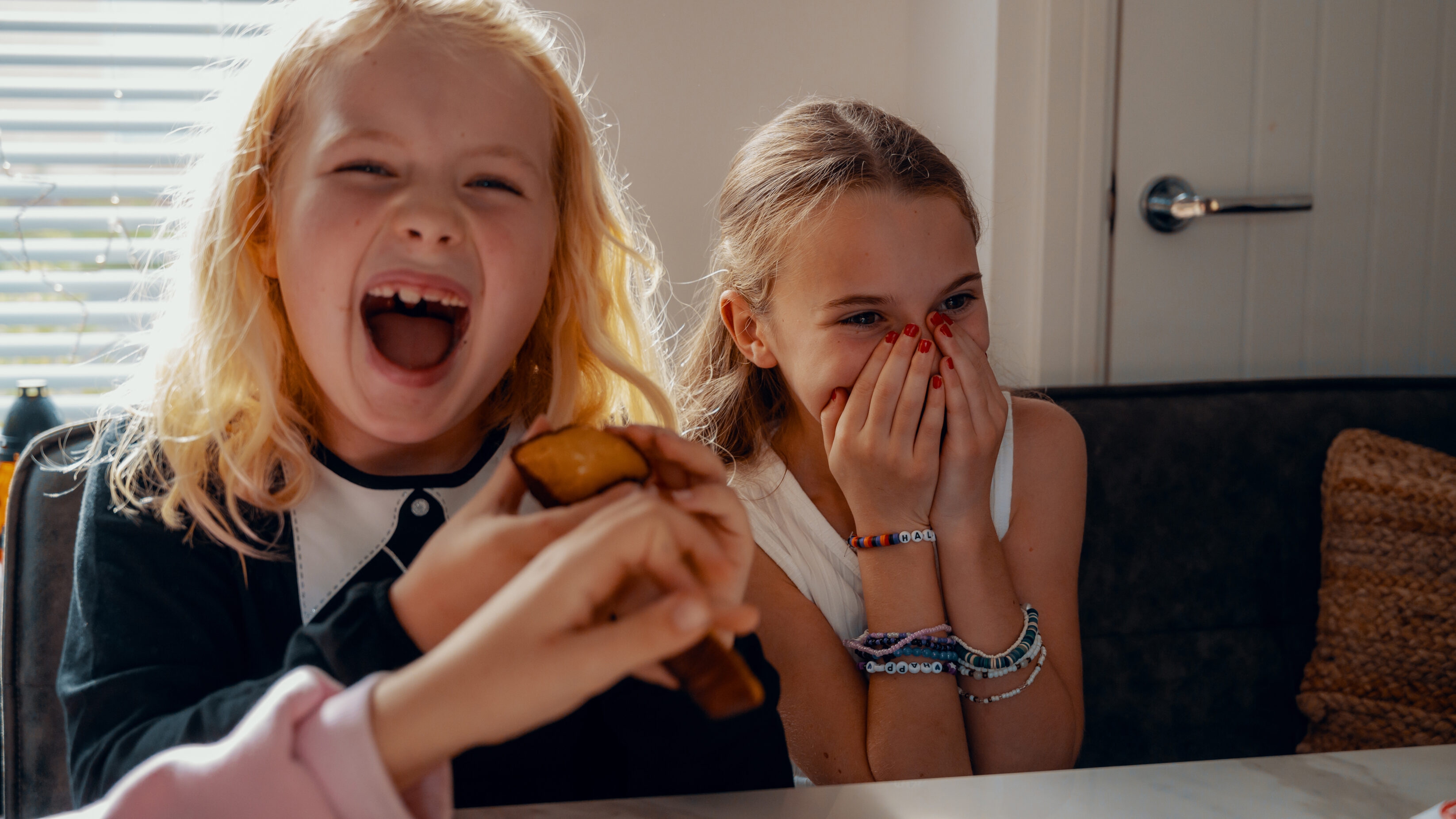 Two girls around ten years of age, smiling, laughing and sharing white chocolate brownies