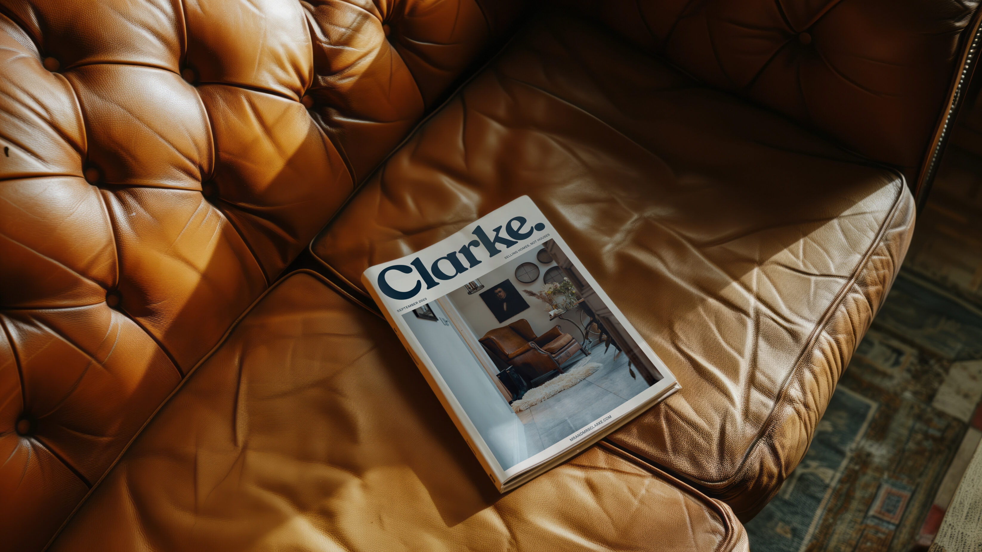 Brochure, showing the cover and a beautiful interior on it. The brochure is sitting on a brown leather sofa.