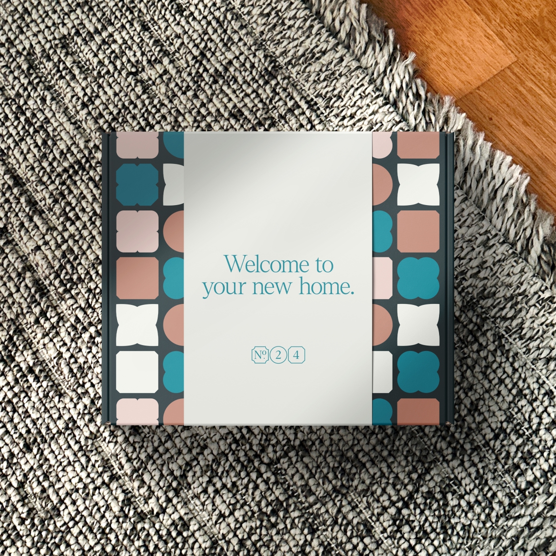 A 'welcome to your new home' box, with the brand pattern in the background, a branded sleeve, laying on a light grey rug.