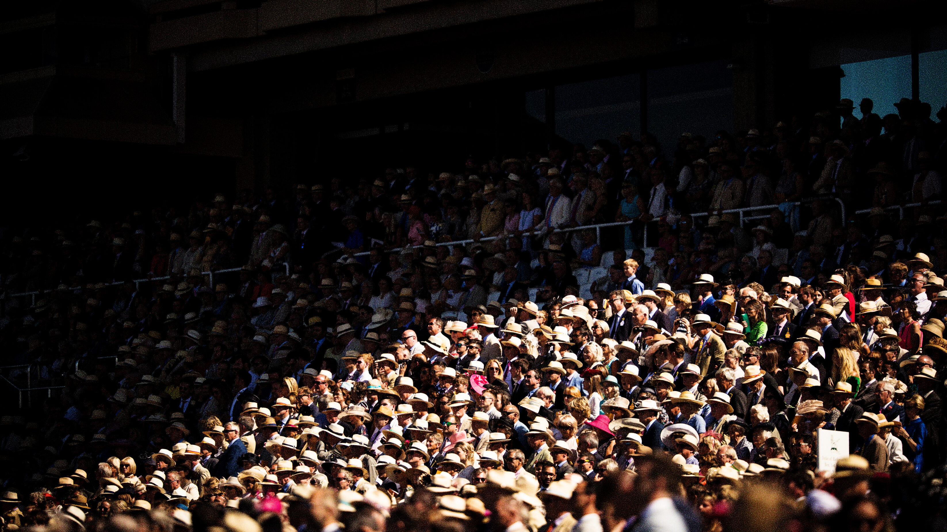 A crowd watching a horse race - they are very much on brand with their fancy hats