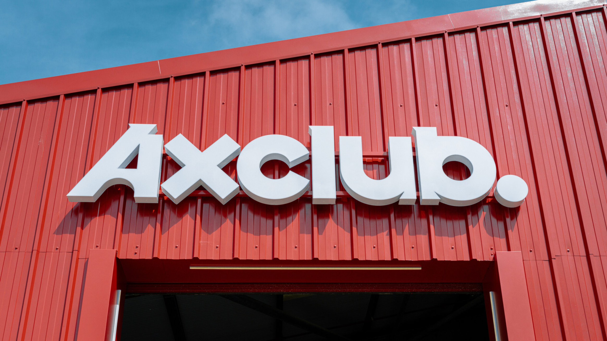 AxClub entrance sign in white, on the red metal building exterior.